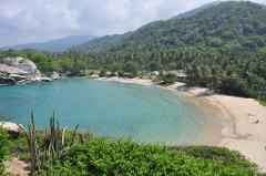 A beautiful tropical beach with turquoise water and lush green vegetation against a backdrop of mountains.