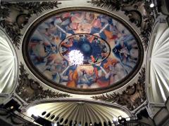 An ornate oval ceiling mural with a chandelier at the center, decorated with classic architectural details and a painted scene of figures and clouds.