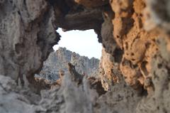 A unique perspective through a rocky aperture reveals a landscape of jagged, barren peaks under a pale sky, creating a surreal and otherworldly scene.