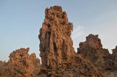 A close-up shot shows a group of tall, intricate brown rock formations under a pale blue sky.