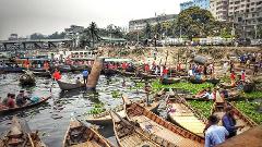 A bustling river scene with numerous boats filled with people amidst lush greenery and urban infrastructure in the background.