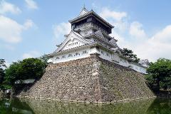 A traditional Japanese castle with a stone foundation surrounded by a moat under a bright sky.
