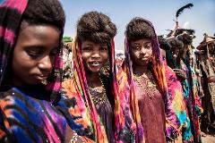 A group of Wodaabe women are lined up for a beauty pageant during the Gerewol festival, wearing colorful robes and with traditional hairstyles.