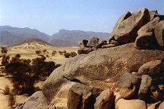 Eine felsige, bergige Wüstenlandschaft mit alten Petroglyphen, die im Vordergrund in einen großen Felsbrocken gehauen sind.