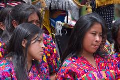 A group of indigenous women wearing colorful traditional clothing are seen in a close-up shot, with intricate details of their garments and expressions visible.