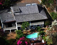 An aerial view showcases a building with a pool and surrounding lush greenery, creating a tropical scene.