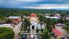 Aerial view of a town featuring a white church with a red dome surrounded by lush green trees and parked cars.