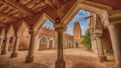 A courtyard with a tower in the background is framed by columns and arches in a traditional mud-brick building.