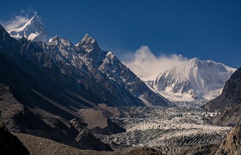 A stunning landscape featuring snow-capped mountains, a glacial valley, and a clear blue sky.