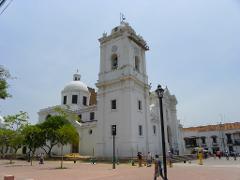 Parque Nacional Natural Tayrona Tour de 2 días desde Cartagena A white cathedral with a tall bell tower stands in a sunny plaza, with people walking around.
