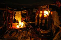 Inside a dimly lit tent, various textiles and artifacts are displayed under the warm glow of lanterns, creating a mysterious and inviting atmosphere.