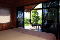 This photo showcases a bedroom with a large sliding glass door leading to a wooden deck with chairs, offering views of lush greenery.