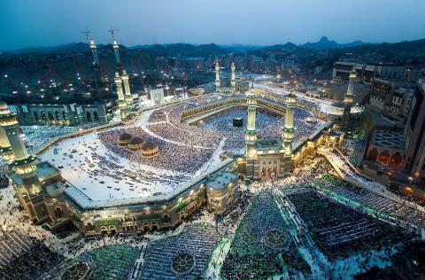 Aerial view of the Masjid al-Haram in Mecca, Saudi Arabia, crowded with pilgrims, with the Kaaba at its center, under a twilight sky.