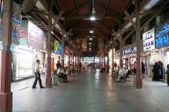 This image captures a lively pedestrian walkway lined with shops, many of them jewelers, beneath a wooden structure, bustling with people going about their day.