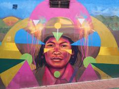 A vibrant mural on a building depicts a person with geometric shapes and colorful, dreamlike elements around them.