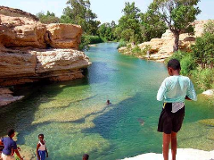 A picturesque scene with a group of children near a river surrounded by rock formations and trees in a sunny, outdoor setting.