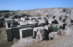 This image depicts ancient ruins with rectangular brick structures, possibly from an archaeological site, set in a desert environment under a clear sky.