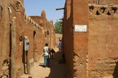 A street in an African village, with children and buildings made of mud, under a bright sun.