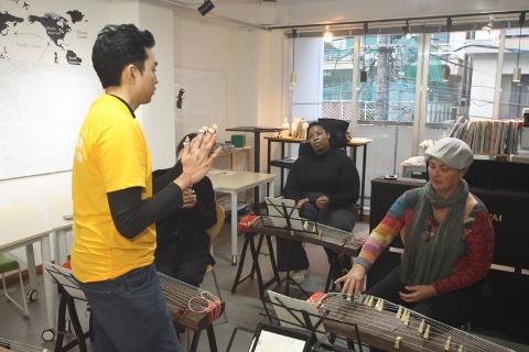 A man in a yellow shirt teaches two women how to play the koto during a cultural study program in Hiroshima.