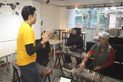 A man in a yellow shirt teaches two women how to play the koto during a cultural study program in Hiroshima.
