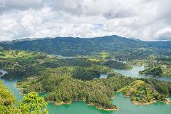 A scenic view of a lake surrounded by lush green hills and mountains under a cloudy sky.