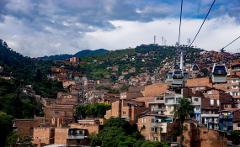 A densely populated hillside with brick buildings is seen, with a cable car system running overhead.