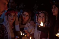 Illuminated by candlelight, a group of women wearing headscarves and flower crowns, stand together in a dimly lit space, creating an intimate and mysterious scene.
