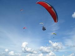 A group of paragliders are soaring through the clear blue sky, dotted with puffy white clouds.