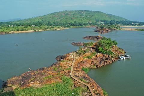 Forfait de voyage à Bangui avec visa à l'arrivée pour la République centrafricaine A wide river winds around a rocky island with a stone pathway, leading to a lush green hill topped with scattered buildings.