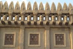 This is a close-up of a building with traditional architecture, featuring a castellated parapet, decorative windows, and rustic construction.