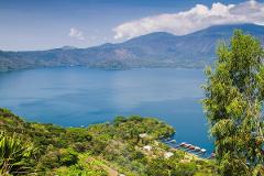 A scenic view of a blue lake surrounded by lush green hills and mountains under a partly cloudy sky.