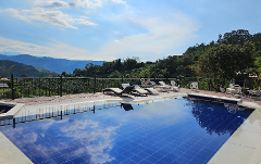 A tranquil swimming pool reflects the sky, with lounge chairs and a scenic mountain backdrop.