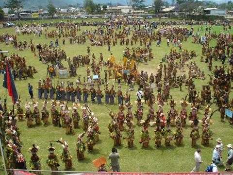 A large group of people in traditional costumes gather in a field for the Goroka Show Festival in Papua New Guinea.
