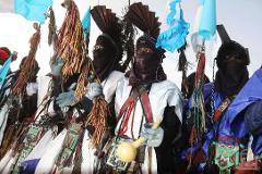 A group of colorfully dressed Tuareg men participate in the Bianou Festival in Niger, with traditional clothing, decorative items, and face coverings.
