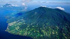 An aerial view of Isla de Ometepe in Nicaragua showcases the lush green landscape, featuring the towering Volcán Concepción and Volcán Maderas, nestled amidst a clear blue sky and water.