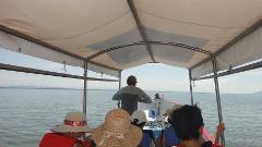 A group of people are riding on a boat on a calm body of water under a covered canopy, with a person steering the boat in the front.