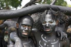 Two men painted black and white pose for a close-up portrait during a cultural event, with the man on the left smiling.