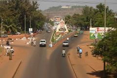 An aerial view of a city street in Africa, with traffic flowing around a monument in the center and buildings visible in the distance.
