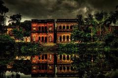 An eerie reflection captures two old brick buildings surrounded by lush greenery, beneath a dramatic, stormy sky.