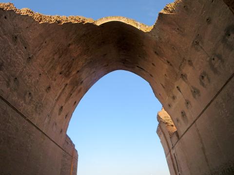 A low-angle shot of a decaying, brick archway framing a bright blue sky, highlighting the structure's age and architectural details.