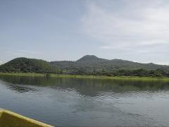 A serene landscape featuring a calm lake reflecting the lush green mountains under a bright, cloudy sky.