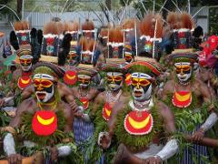 A group of performers in traditional attire, including face paint, feathered headdresses, and leafy costumes, participate in the Mount Hagen Festival & Paiya Show.