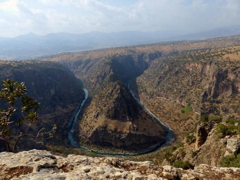 A scenic view of a river meander cutting through a canyon landscape with a rocky foreground and distant mountains.