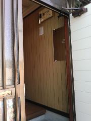 This image shows the entrance to a narrow room with wood-paneled walls, featuring a small mirror and a breaker box.