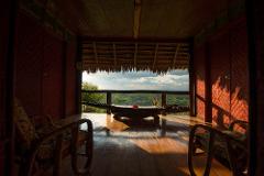The image is a view from a balcony of the Karawari Lodge, featuring wooden chairs, a table shaped like a crocodile, and a panoramic view of the surrounding landscape.