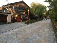 A street in Kyoto, Japan is paved with cobblestones and lined with traditional Japanese buildings and trees.