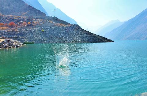 A scenic view of a lake surrounded by mountains, with a splash of water breaking the calm surface and a small boat nestled near the shore.