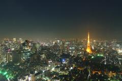 A high-angle, nighttime view of the Tokyo skyline, featuring the illuminated Tokyo Tower as a focal point amidst a sea of brightly lit buildings.