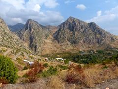 A scenic view of mountainous terrain with winding roads and sparse vegetation under a partly cloudy sky.