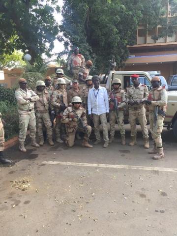 A group of uniformed soldiers stand with rifles in front of a building, surrounding a man in civilian clothes, possibly security forces in Niger.